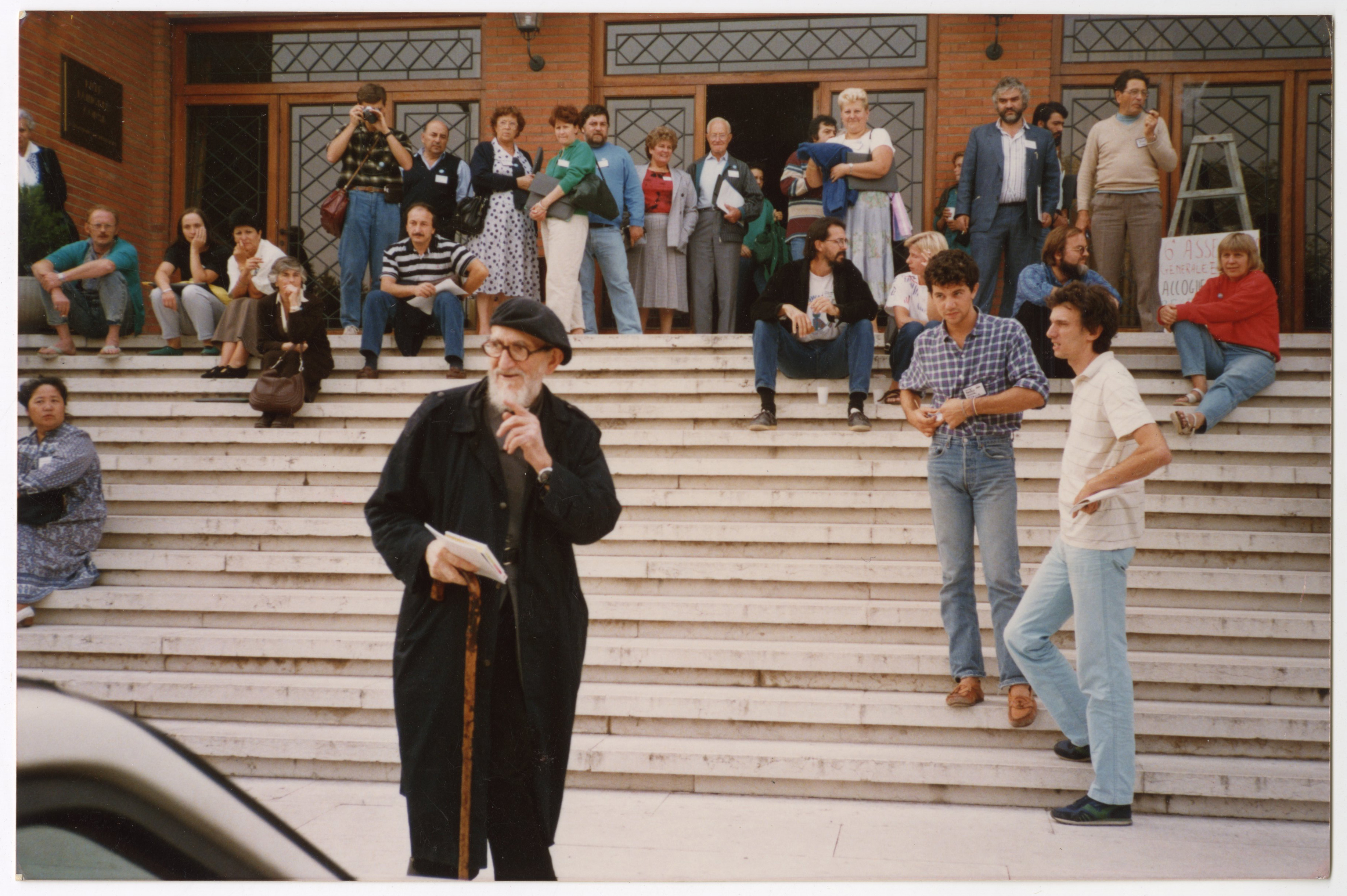 Photographie de l'abbé Pierre et de différents membres d'Emmaüs International devant le lieu de réunion de l'assemblée à Vérone (Italie), 1988.