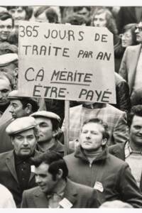Agriculteurs brandissant une pancarte « 365 jours de traite par an, ça mérite être payé » lors d’une manifestation : photographie, sans lieu ni date.