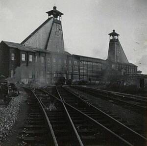 Photographie en noir et blanc de deux chevalements à la mine de Courrières. Des rails sont visibles au premier plan.