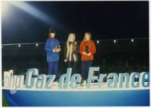 3 jeunes filles sur un podium, devant "Gaz de France" en lettres géantes lumineuses